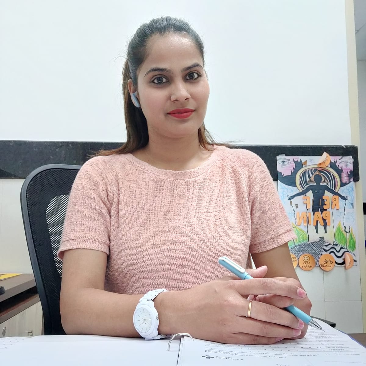 Woman seated at a desk holding a pen beside paperwork