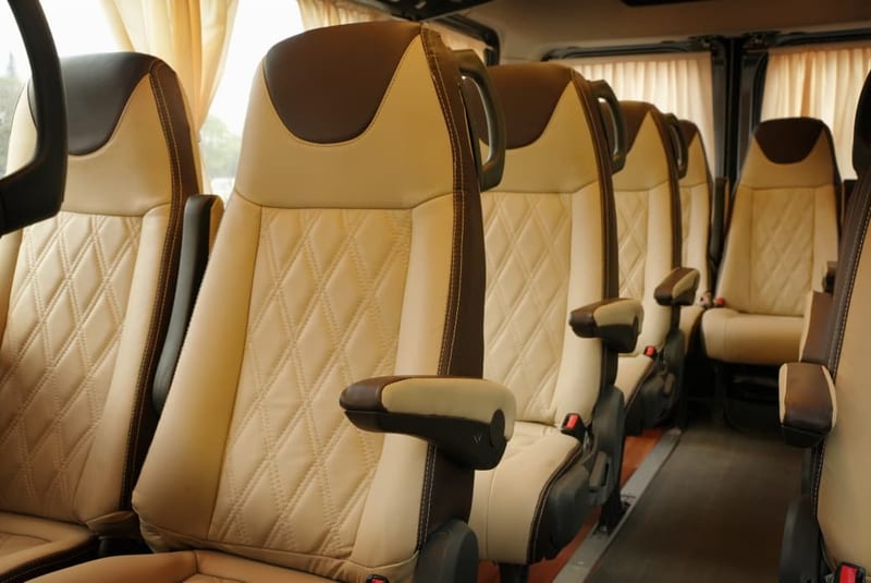 Cream leather passenger seats with armrests and curtains inside an AS Travels vehicle
