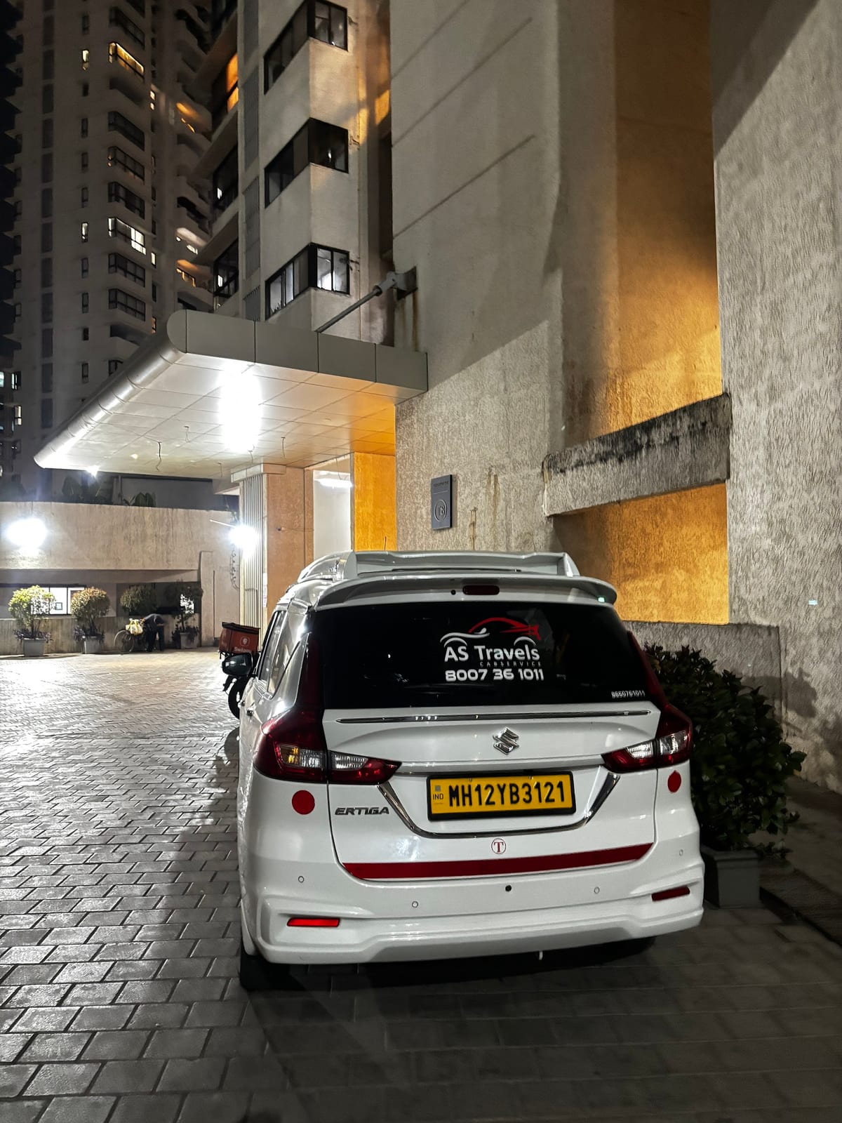 White Suzuki Ertiga parked near a covered building entrance at night
