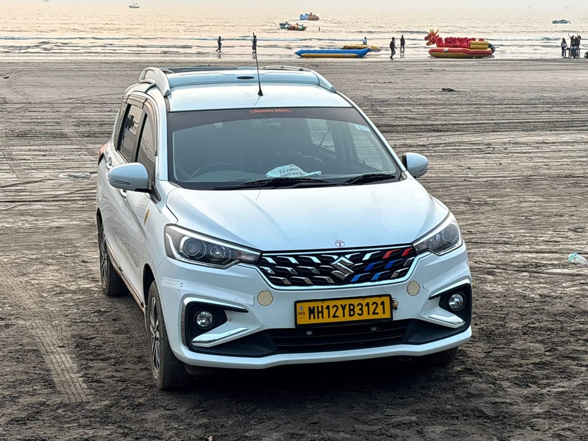White Suzuki car parked on a beach with boats near the water