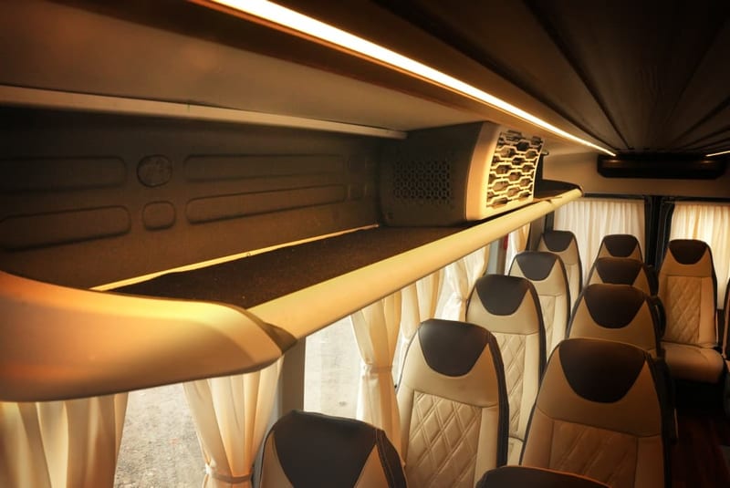 Passenger shuttle interior with upholstered seats, curtains, overhead lighting and luggage shelves