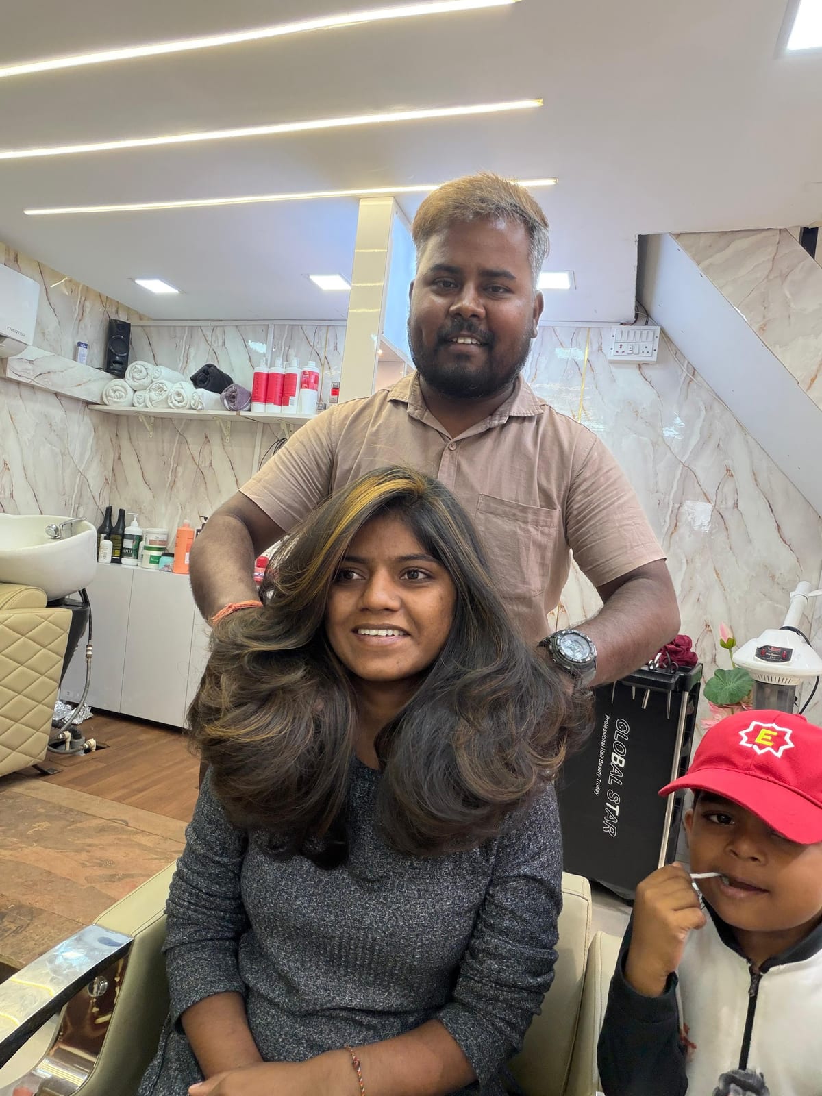 Stylist styling a seated woman's hair with a child beside them