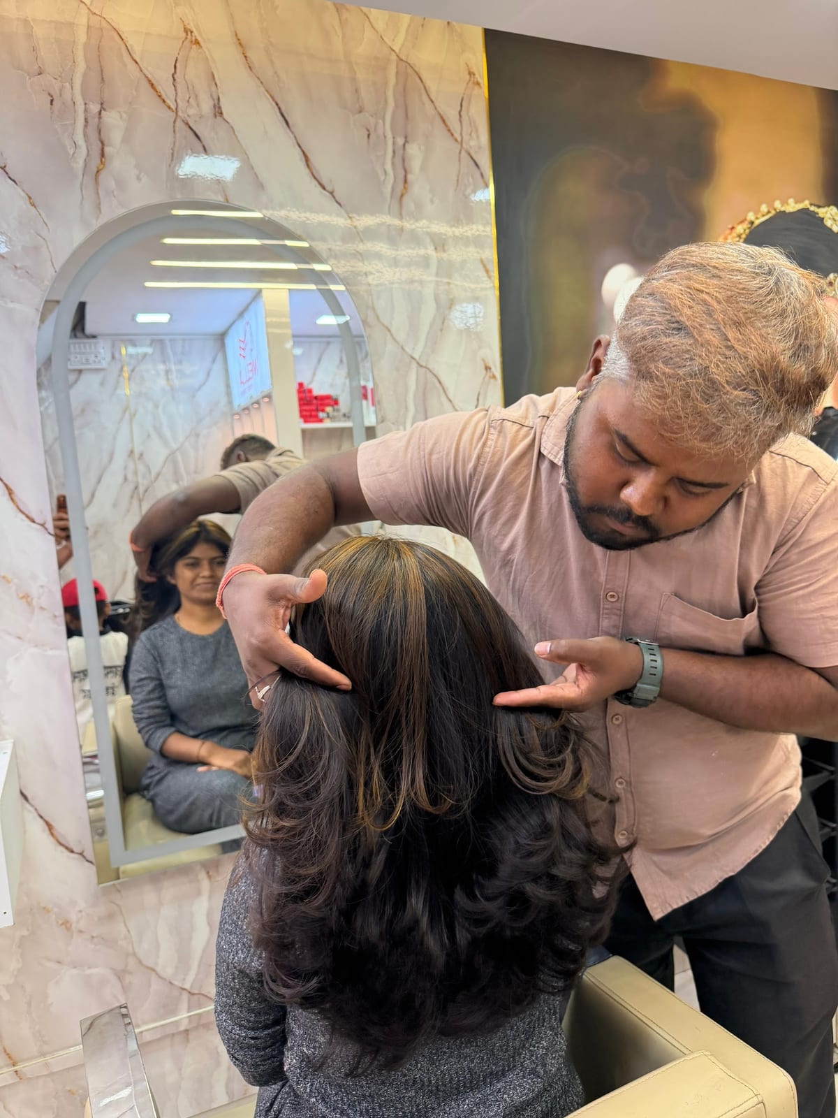 Stylist arranging a client's long hair in front of a salon mirror