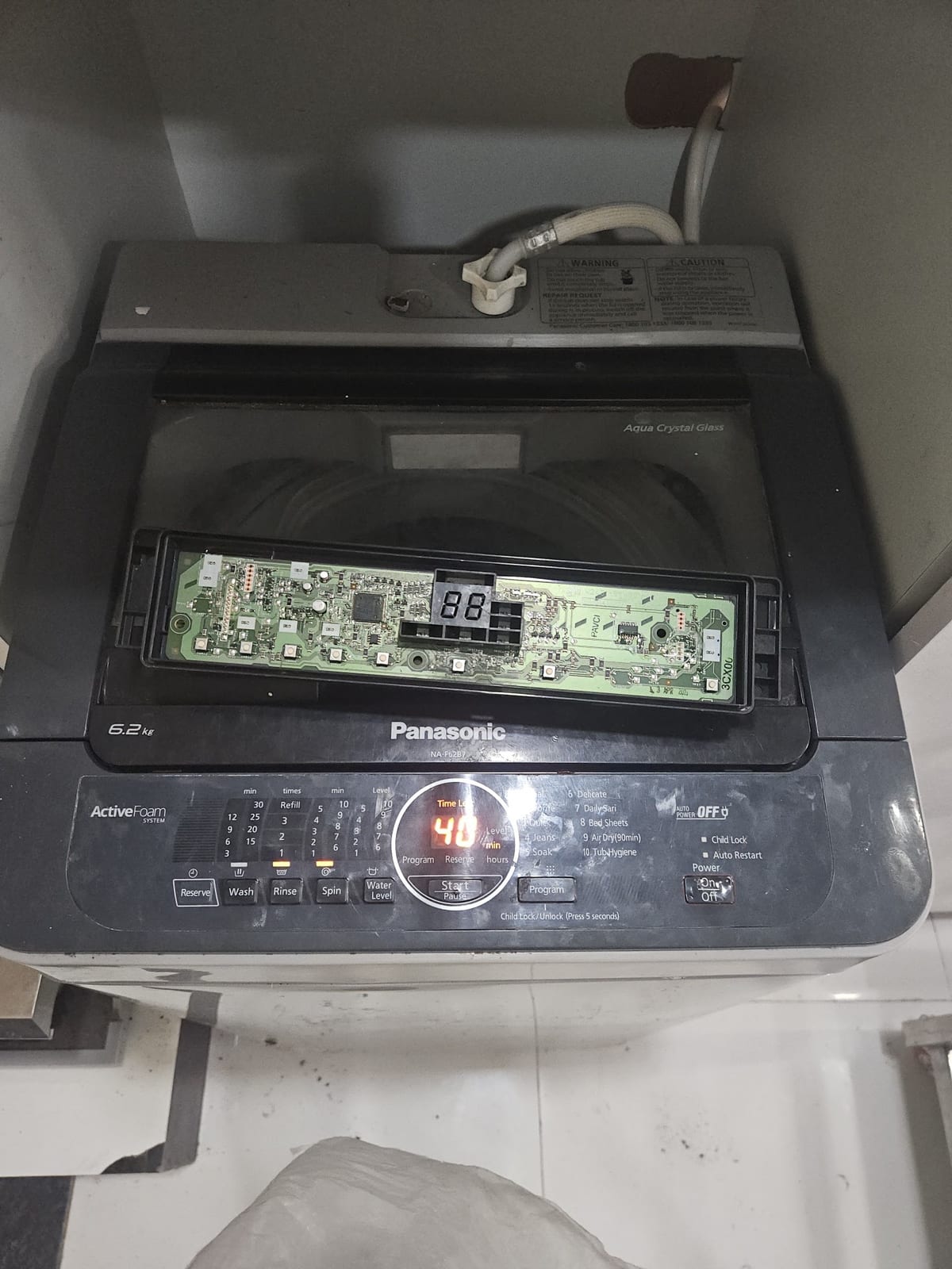 Black Panasonic top-loading washing machine with control panel opened, circuit board exposed