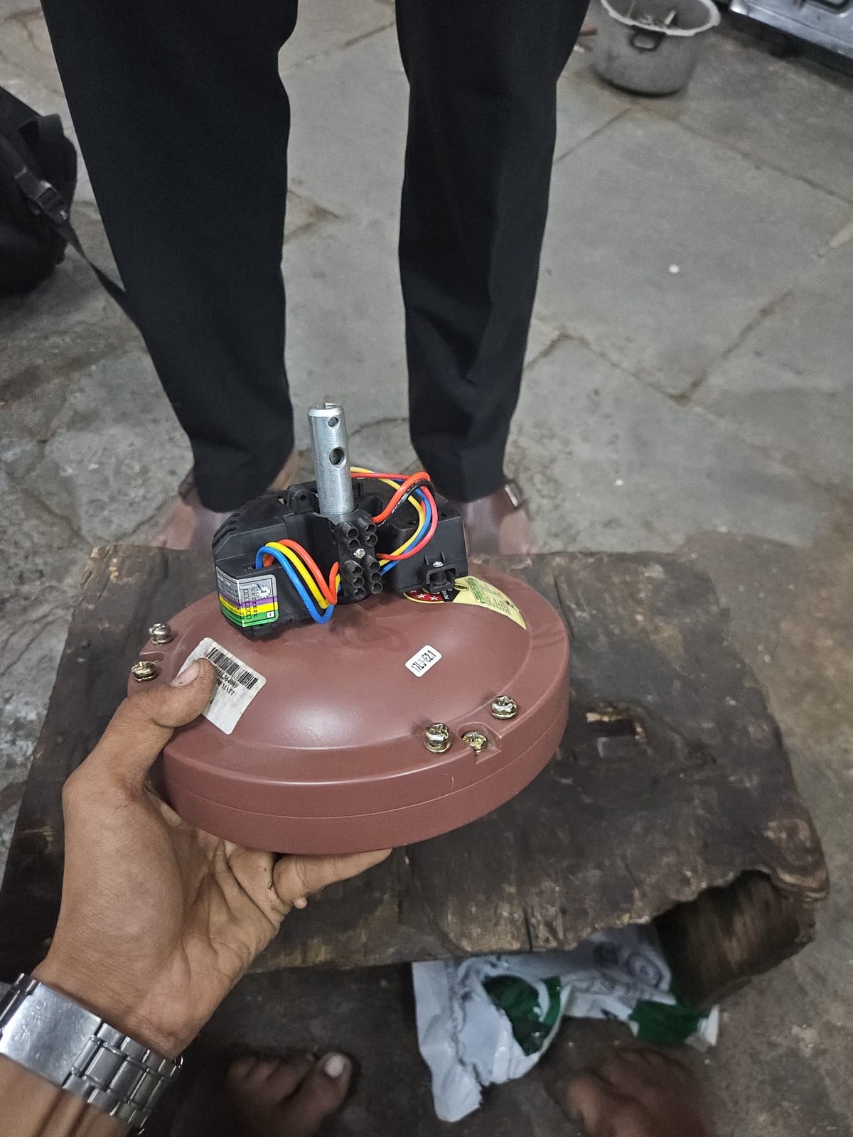 Person holding a round electrical-mechanical component with wiring in a workshop