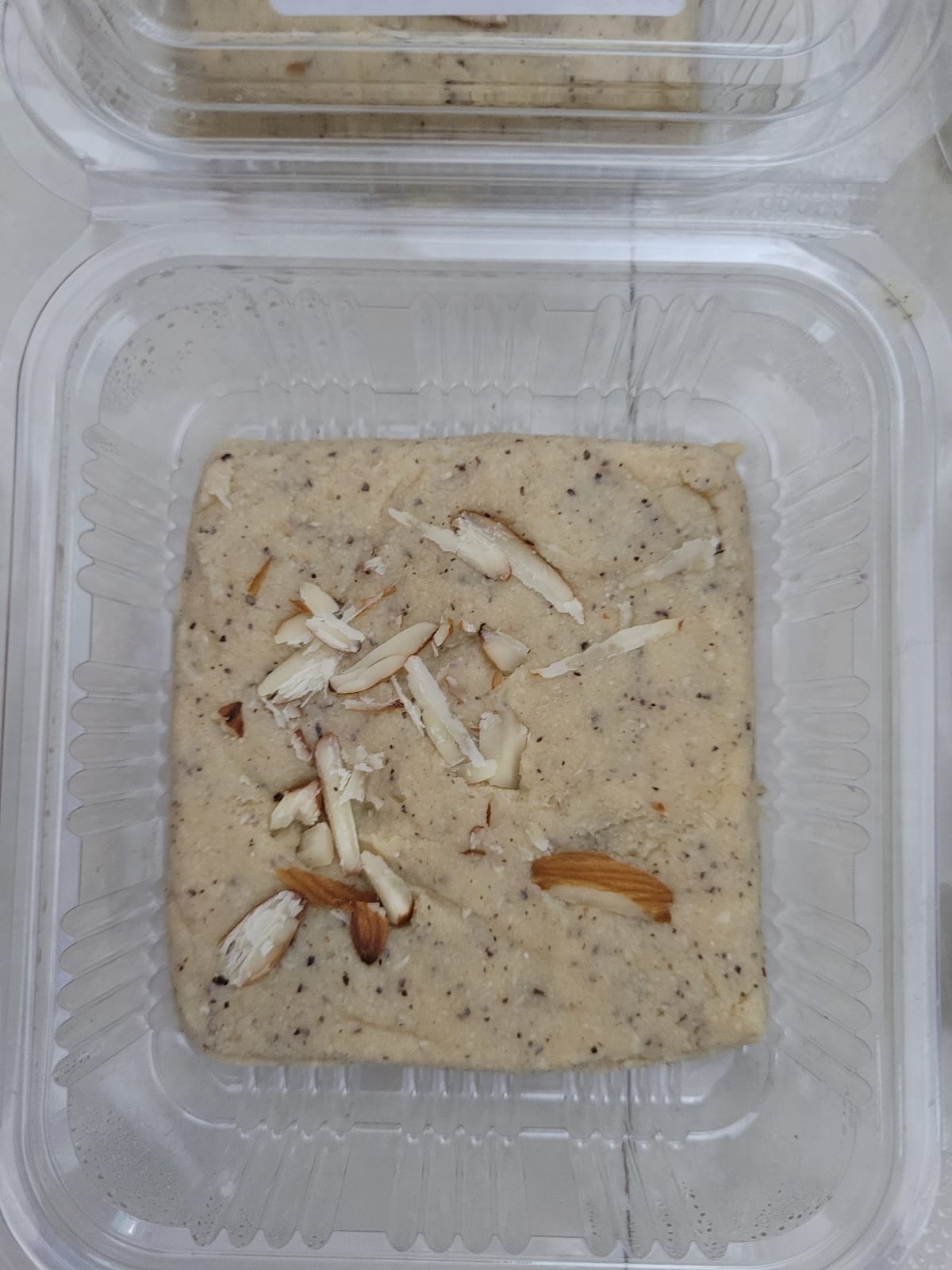 Square beige almond-topped dessert packed in a clear container