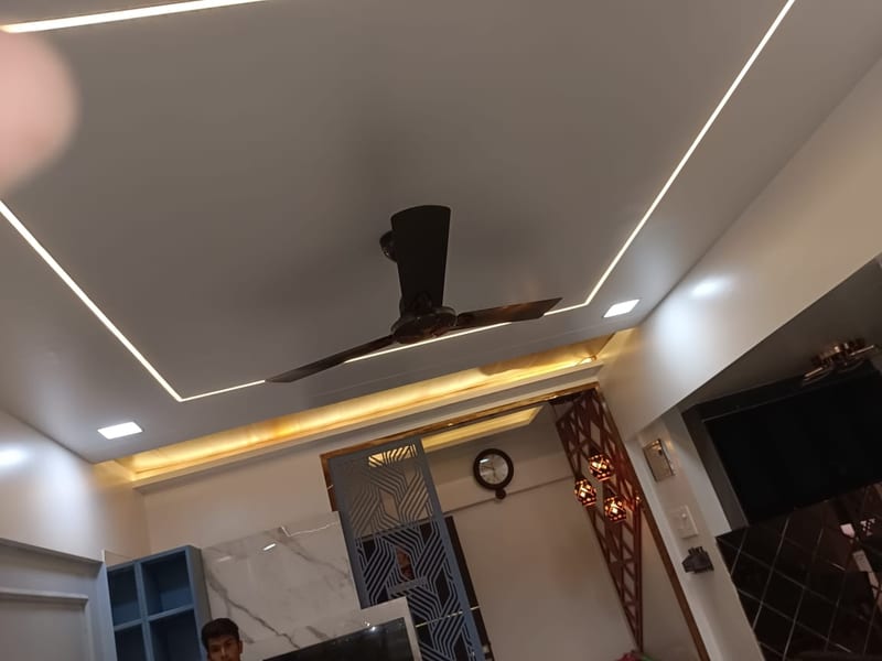 Living room with ceiling fan, wall-mounted TV, shelving and decorative panels