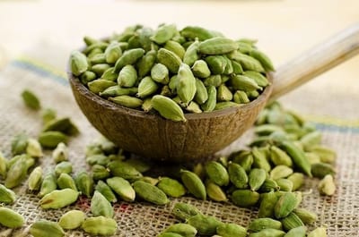 Green cardamom pods in a wooden bowl with loose pods on burlap