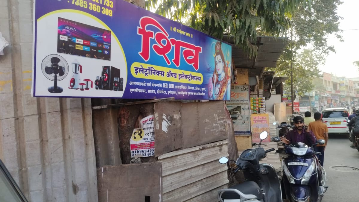 Street-facing electronics shop sign with appliances, scooters and traffic outside