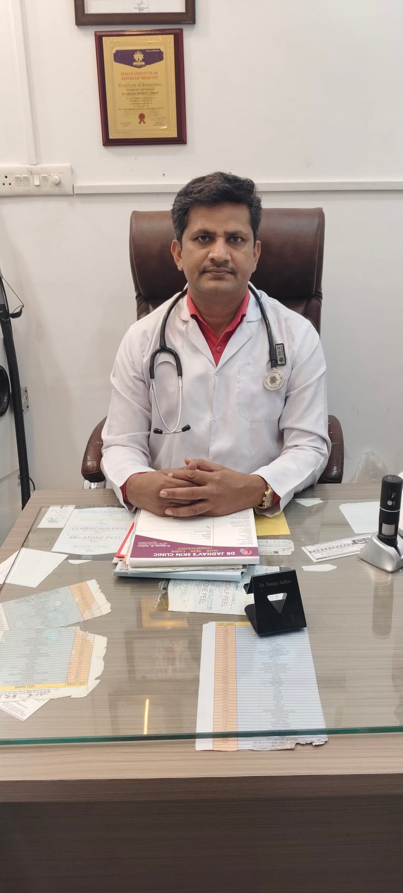 Dermatologist in a white coat and stethoscope seated at a desk