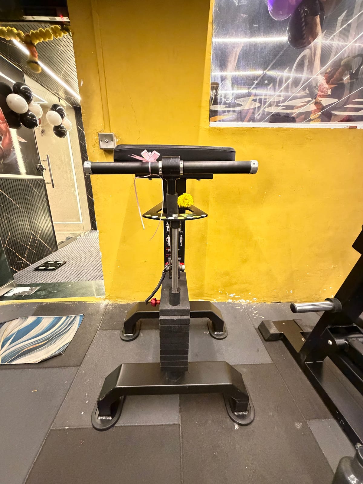 Scooter-like exercise machine in a yellow-walled fitness room with other equipment