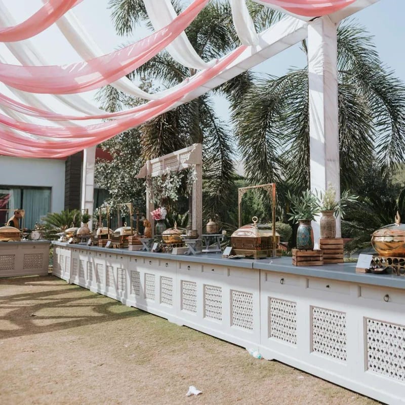 Outdoor buffet station beneath draped pink and white fabric with palm trees