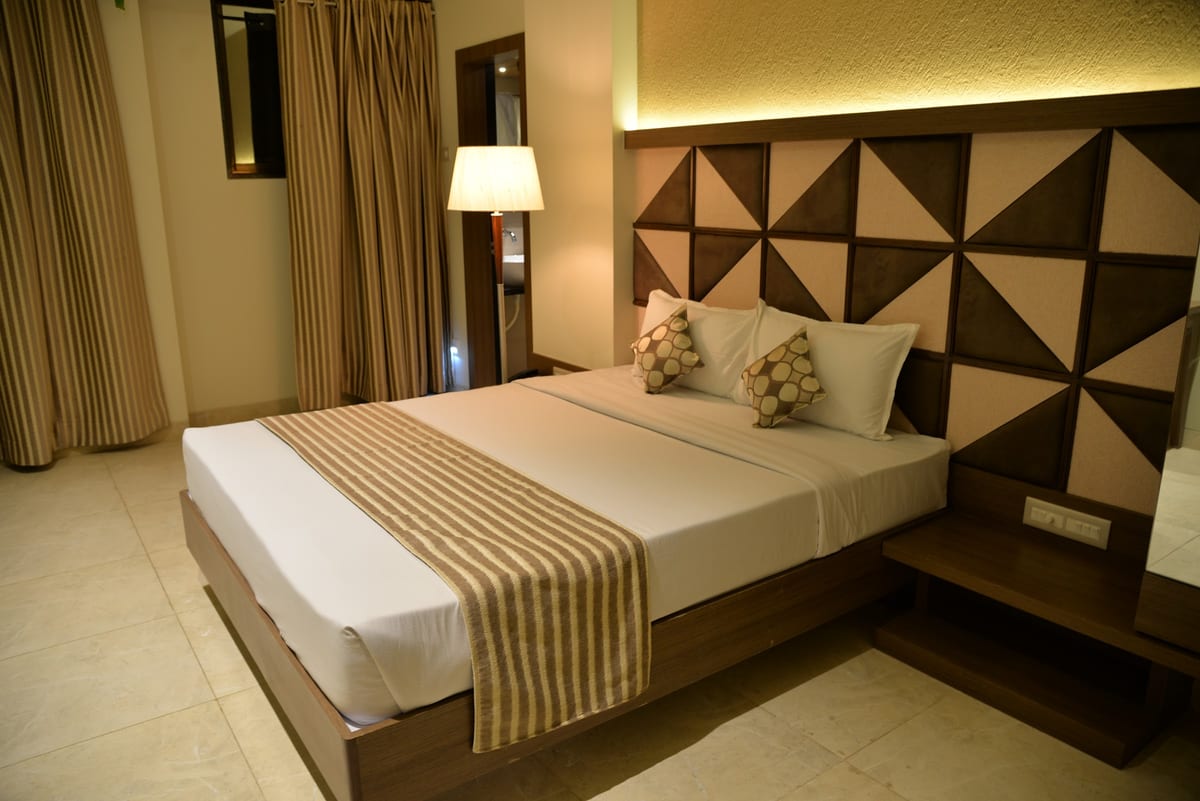 Hotel room with a made bed, geometric headboard, bedside table and floor lamp