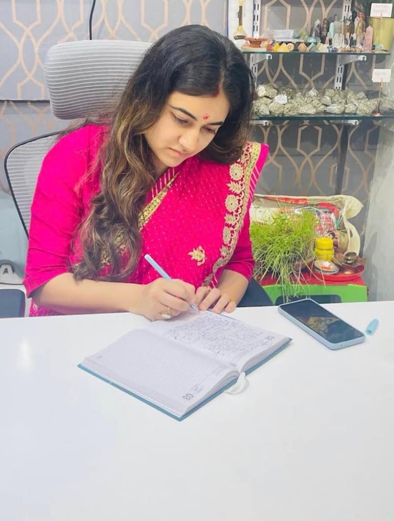 Woman writing in an open notebook at a desk with jewellery displays behind her