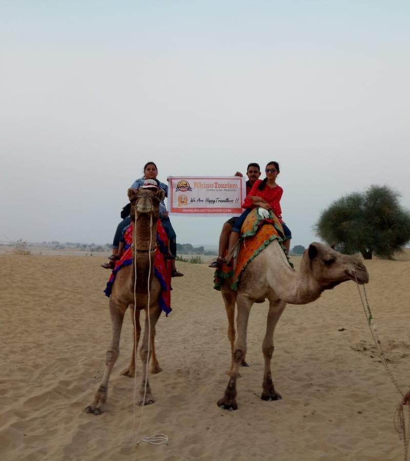 Travelers riding camels across a sandy desert holding a printed sign