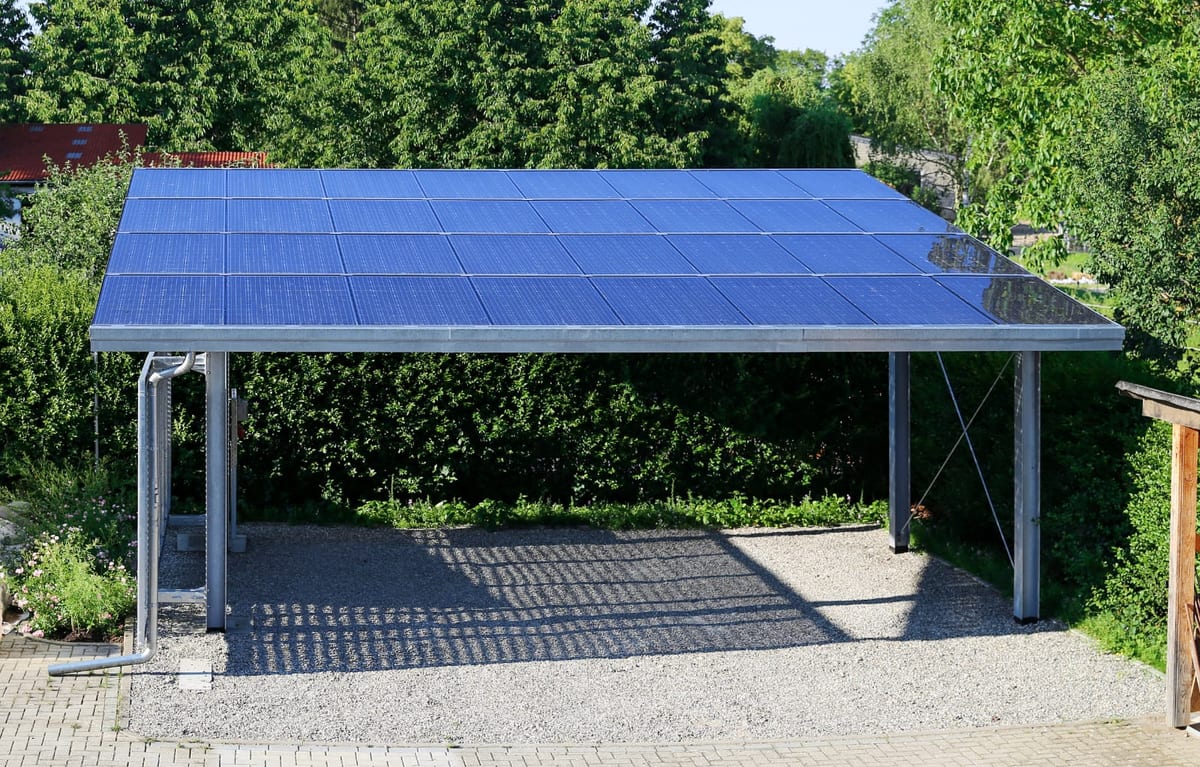 Solar panel carport over a paved parking area lined with trees and shrubs
