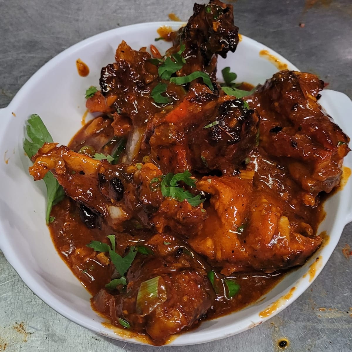 Browned chicken pieces in a glossy reddish-brown sauce with chopped herbs