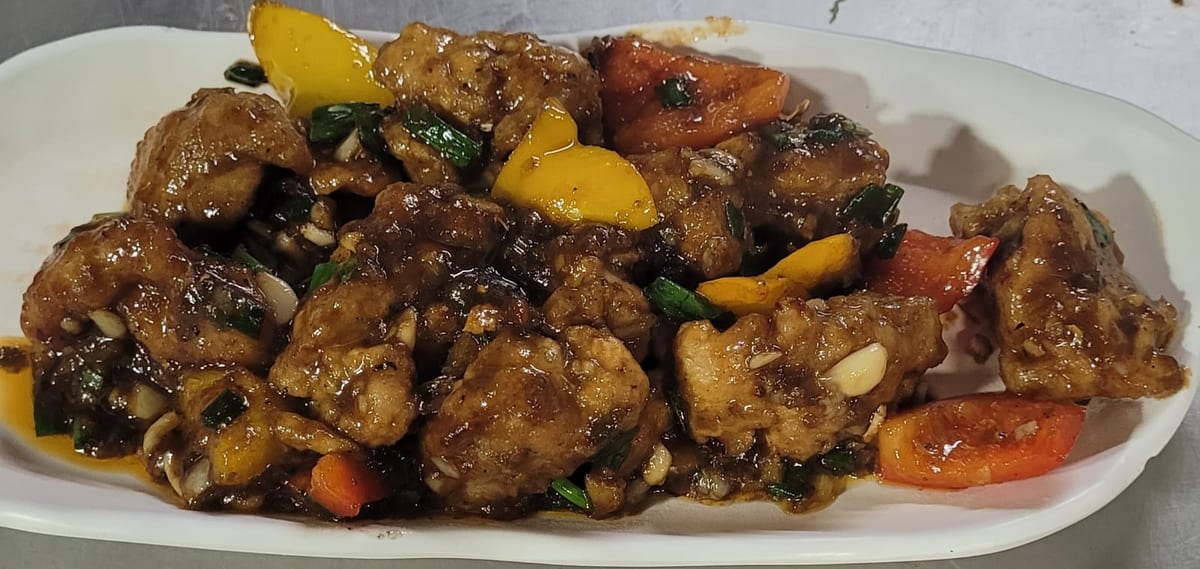 Cooked meat with yellow and red peppers, herbs and seeds on a white oval plate