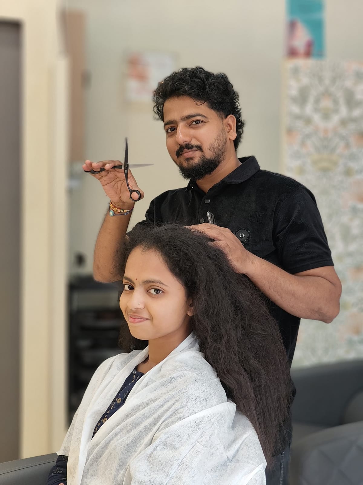 Hairdresser holding scissors while styling a seated woman's long hair