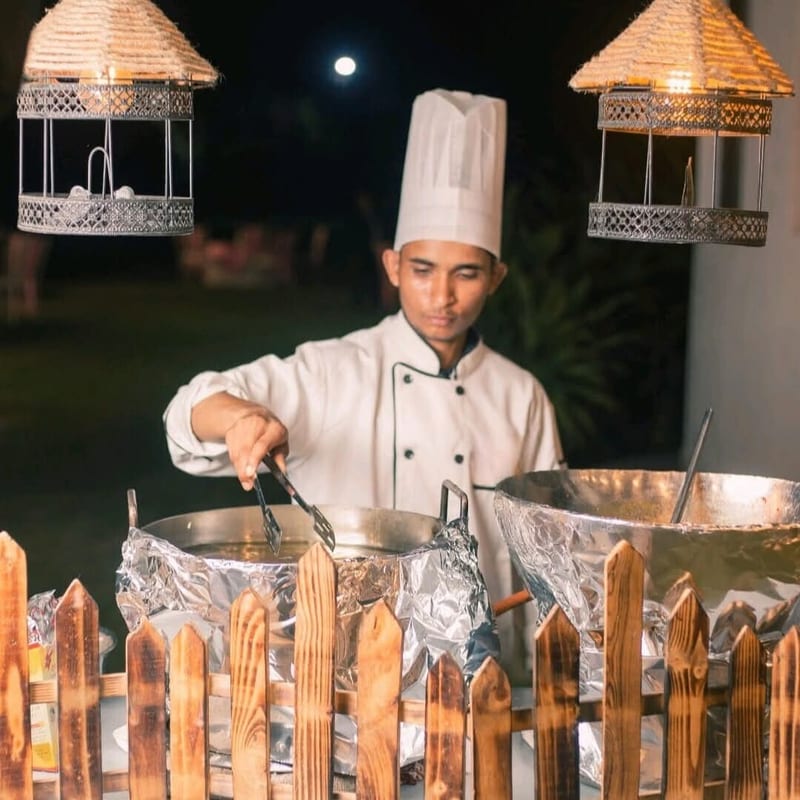 Chef in white uniform cooking at outdoor food stations beneath hanging lanterns