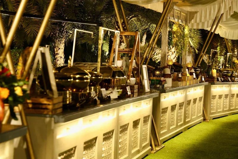 Row of illuminated buffet stations with covered chafing dishes and greenery