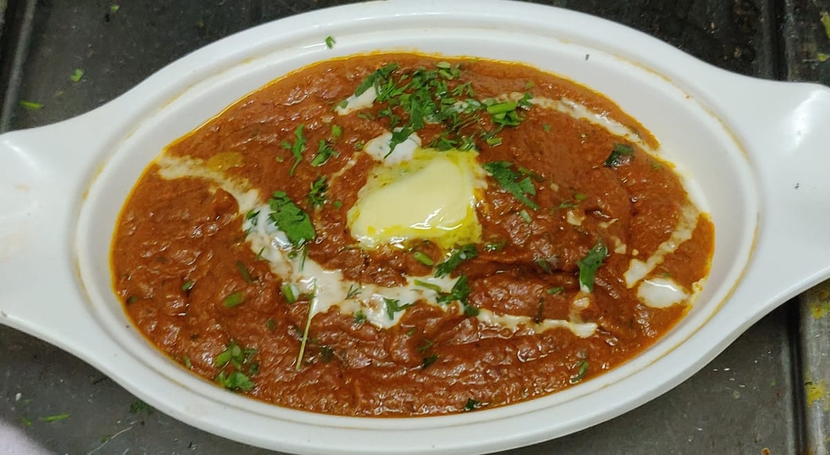 Bowl of red butter chicken curry topped with butter, cream and chopped herbs