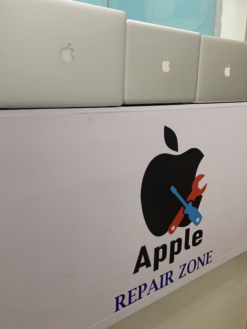 Apple laptops displayed above the counter under the Apple Repair Zone sign