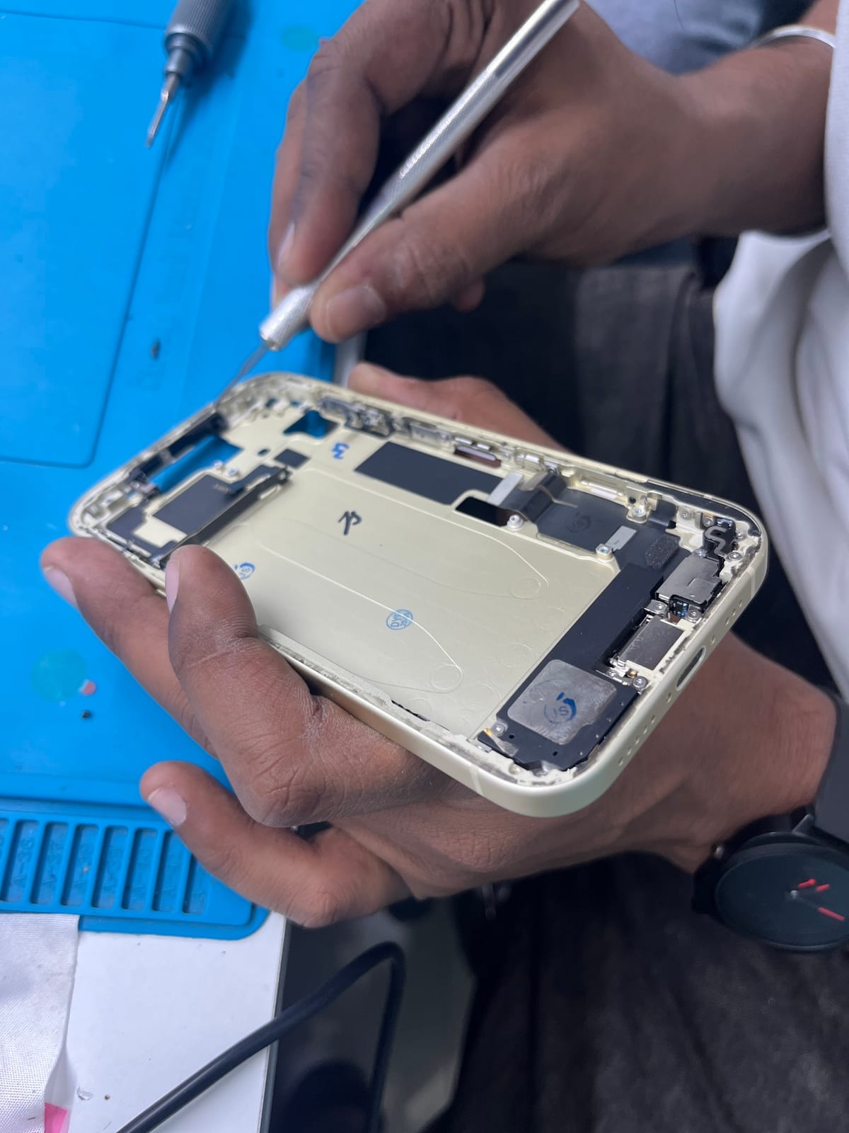 Technician repairing an opened smartphone on a blue work mat
