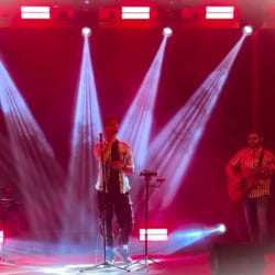 Two musicians performing on a lit stage with microphones and instruments