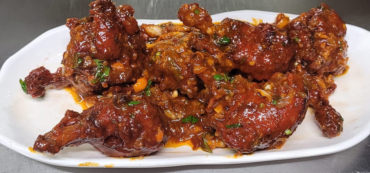 Glazed fried chicken pieces garnished with chopped herbs and nuts on a white plate at Farhang