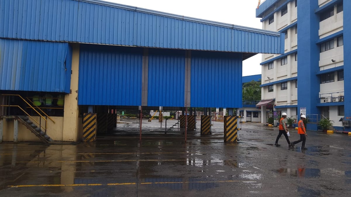 Blue industrial building exterior with a covered loading area on a rainy day