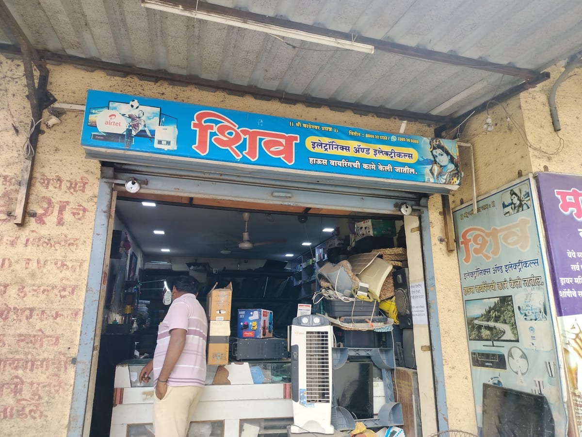 Open shopfront with a blue Hindi sign, shelves, counter and a person inside