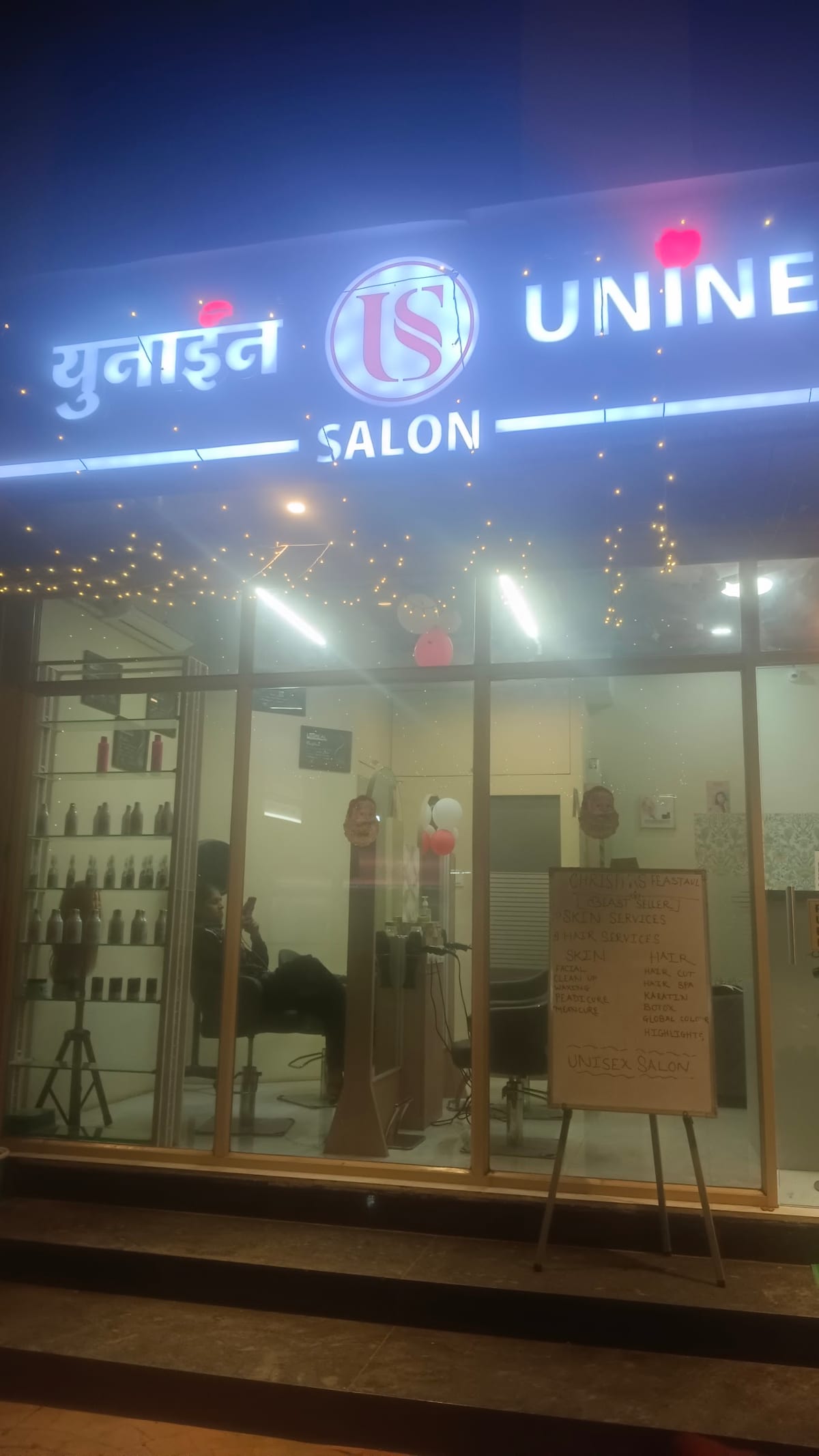 Illuminated Unine Salon storefront at night with glass windows and a sidewalk sign
