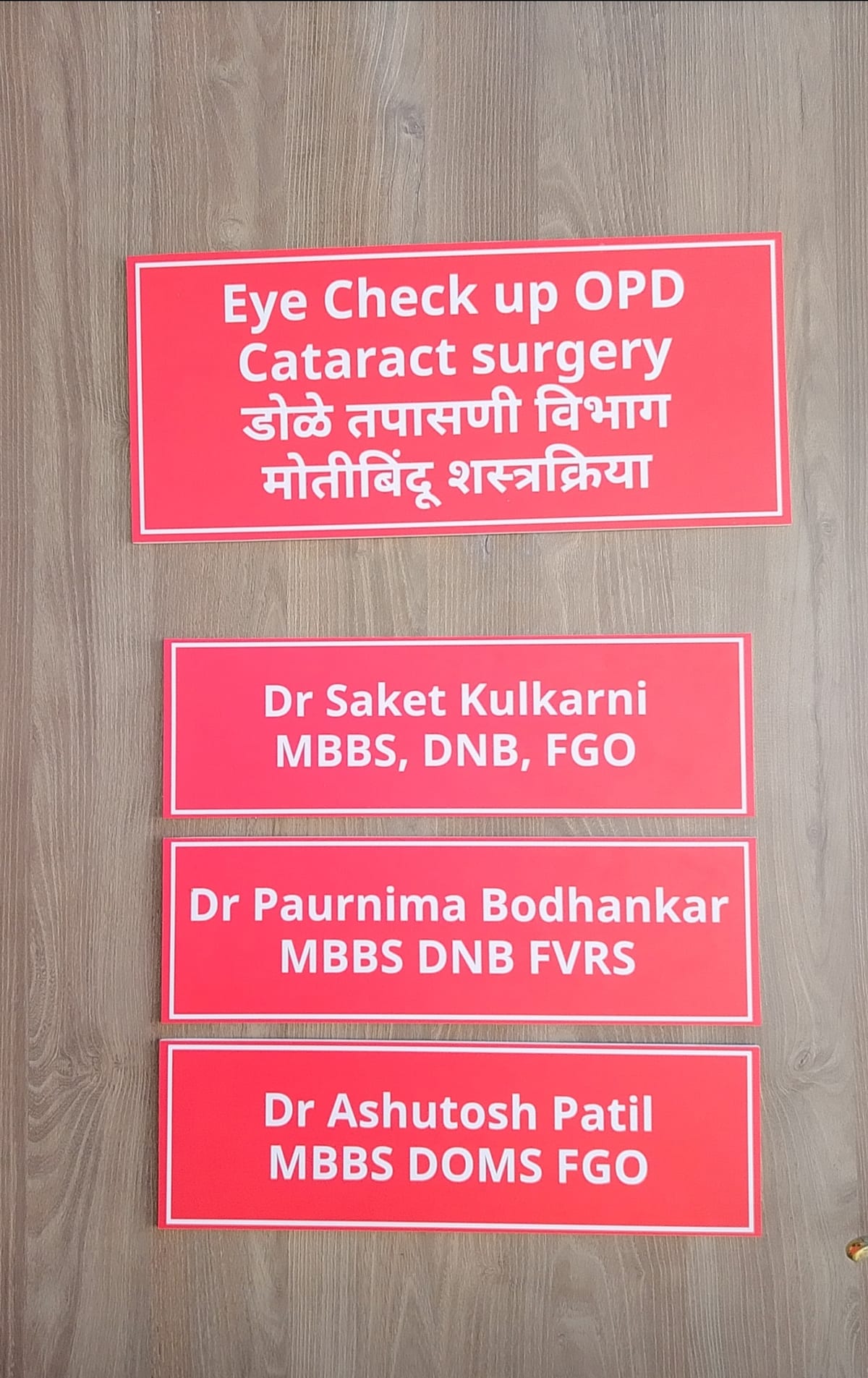Red eye care signs on a wooden door listing check-up and cataract services and doctors