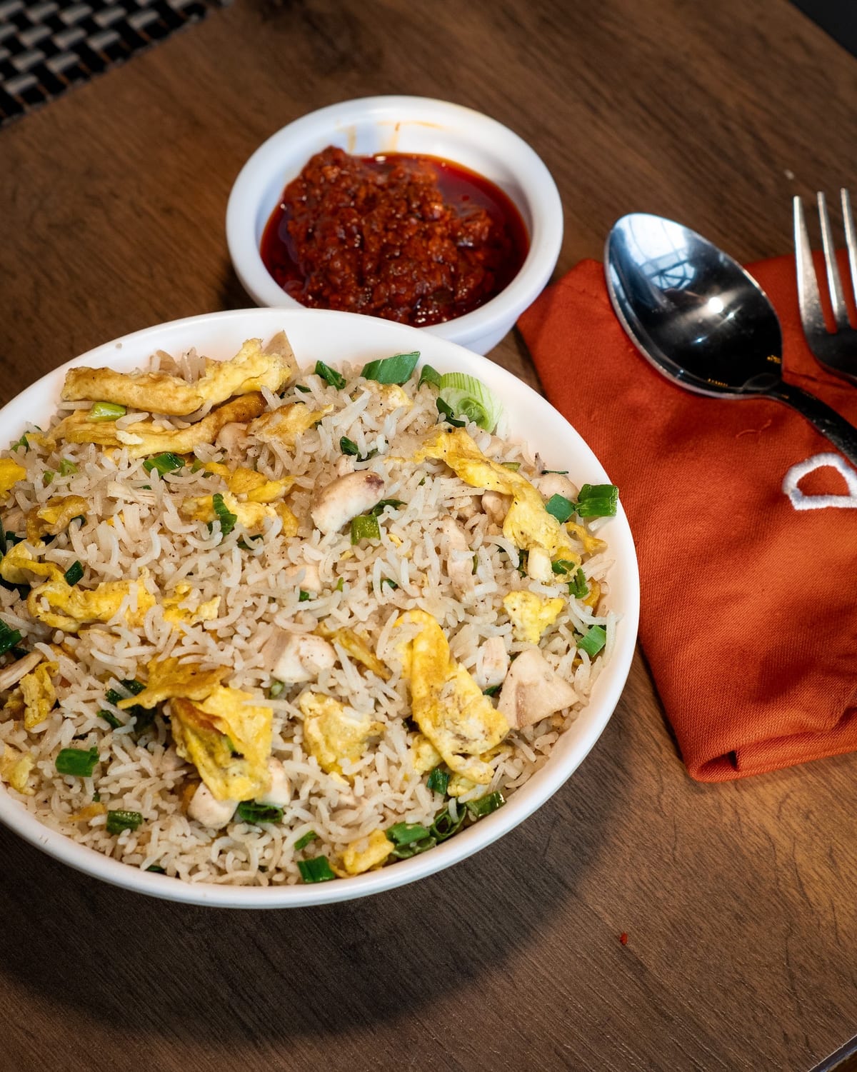 Bowl of fried rice with egg and chicken served with red chili sauce