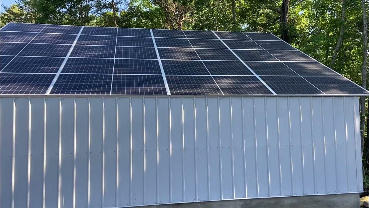 White metal-sided building with a large rooftop solar array among trees