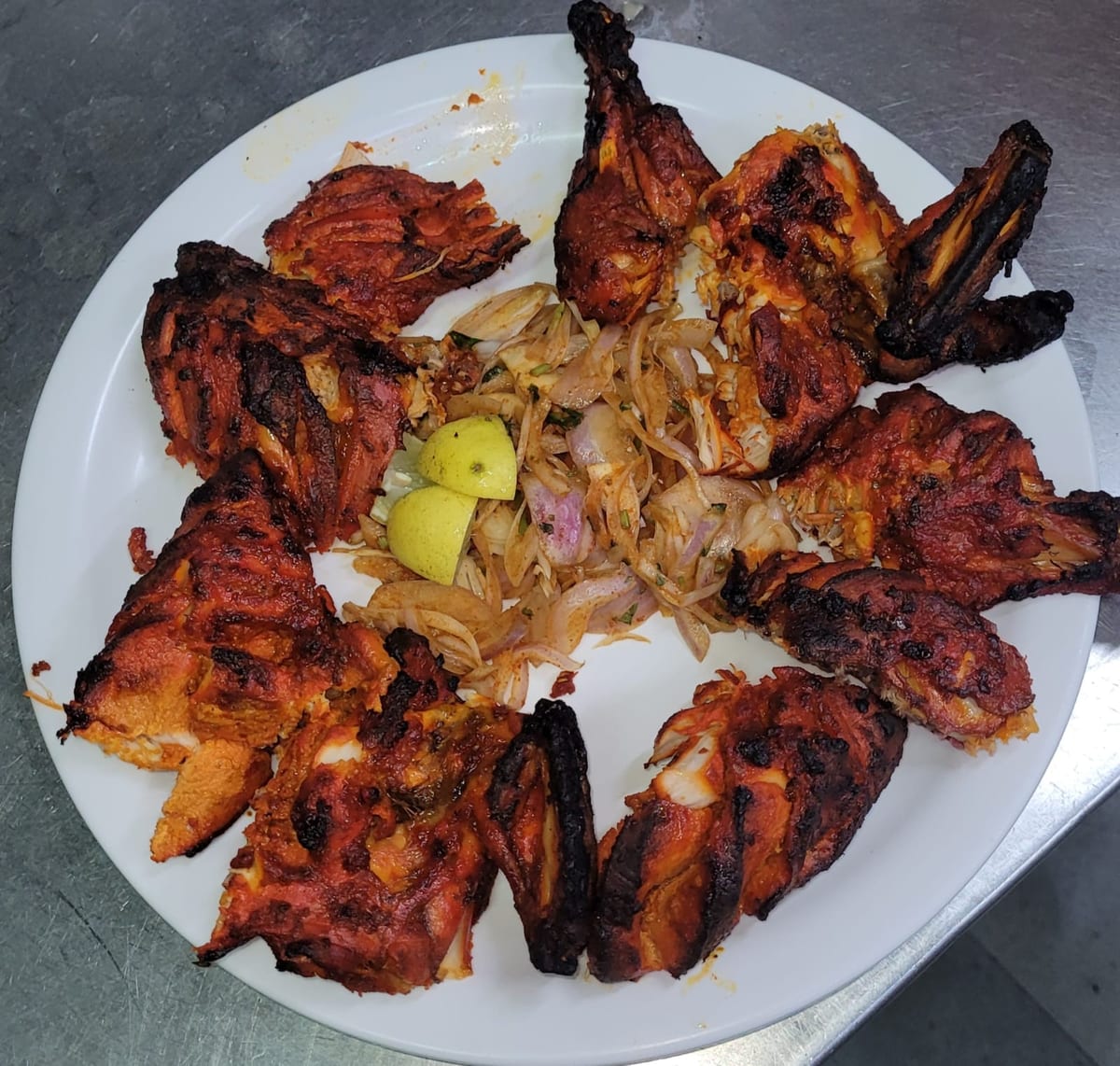 Grilled chicken pieces with sliced onions and lime wedges on a white plate