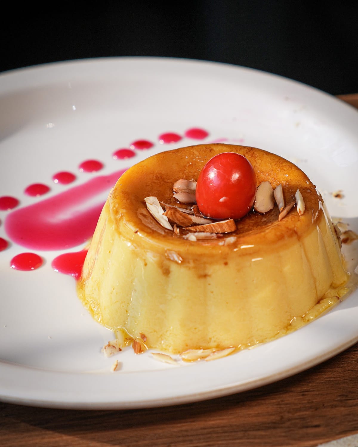 Caramel custard topped with a cherry and sliced almonds on a white plate