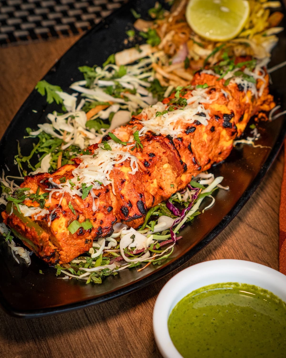 Platter of grilled skewered food on salad with lime and green dipping sauce