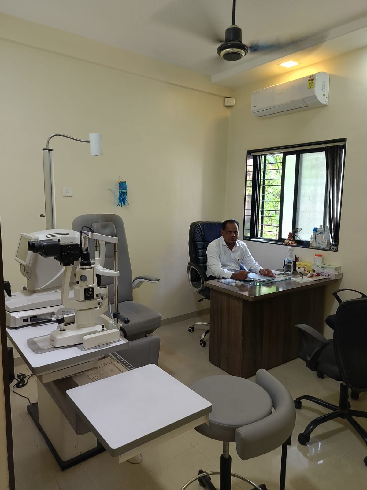 Doctor seated at a desk beside an eye examination machine in a clinic room