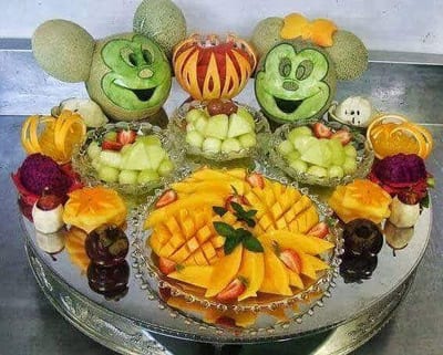 Decorative fruit platter with carved melon faces, fruit bowls and sliced mango
