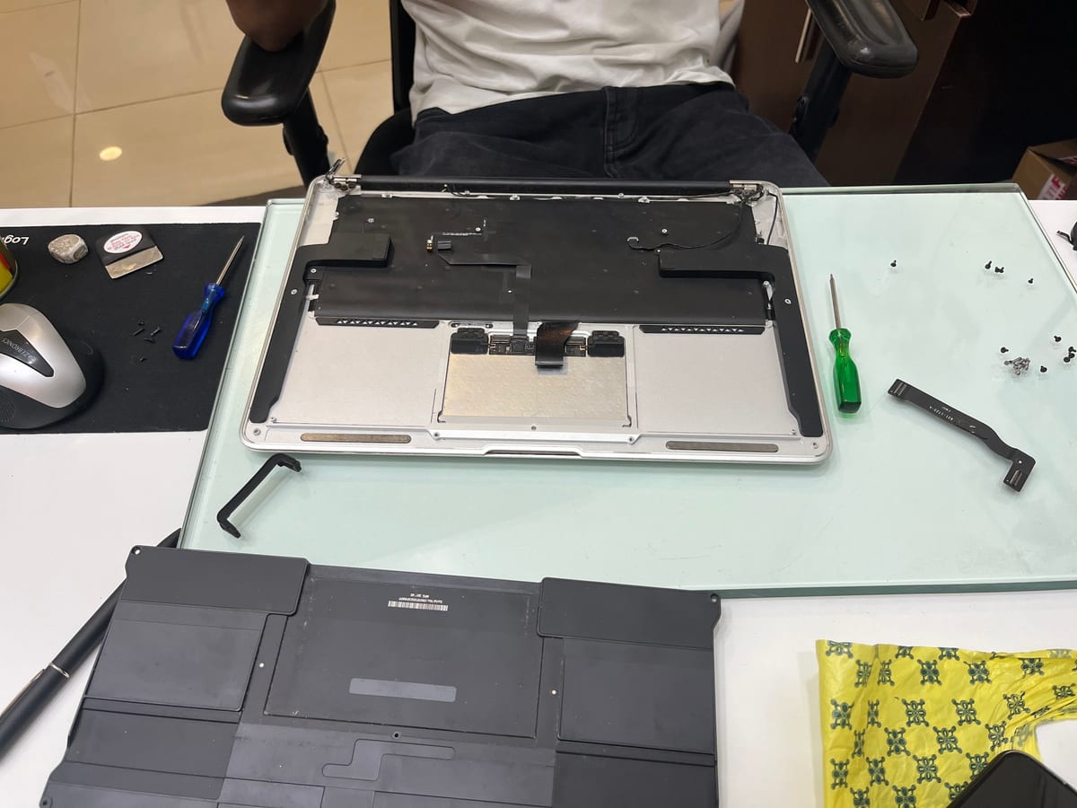 Technician repairing an open laptop with tools and removed internal parts