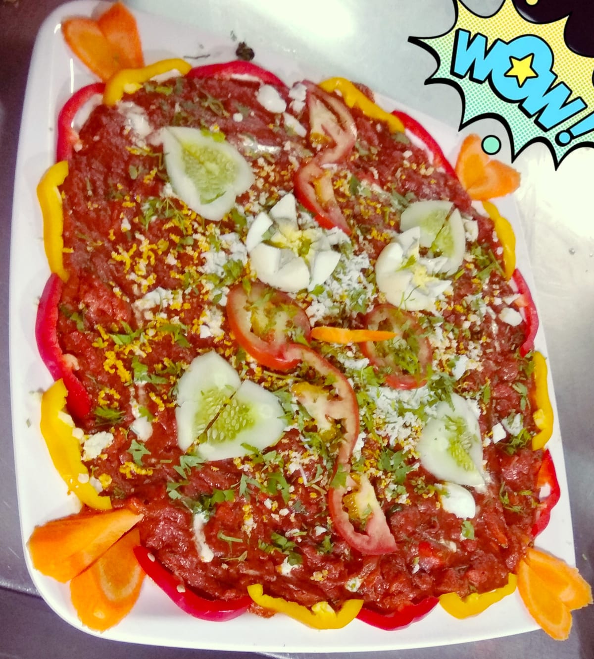 Round savoury dish topped with tomatoes, cucumber, onions, herbs and shredded cheese on a square plate