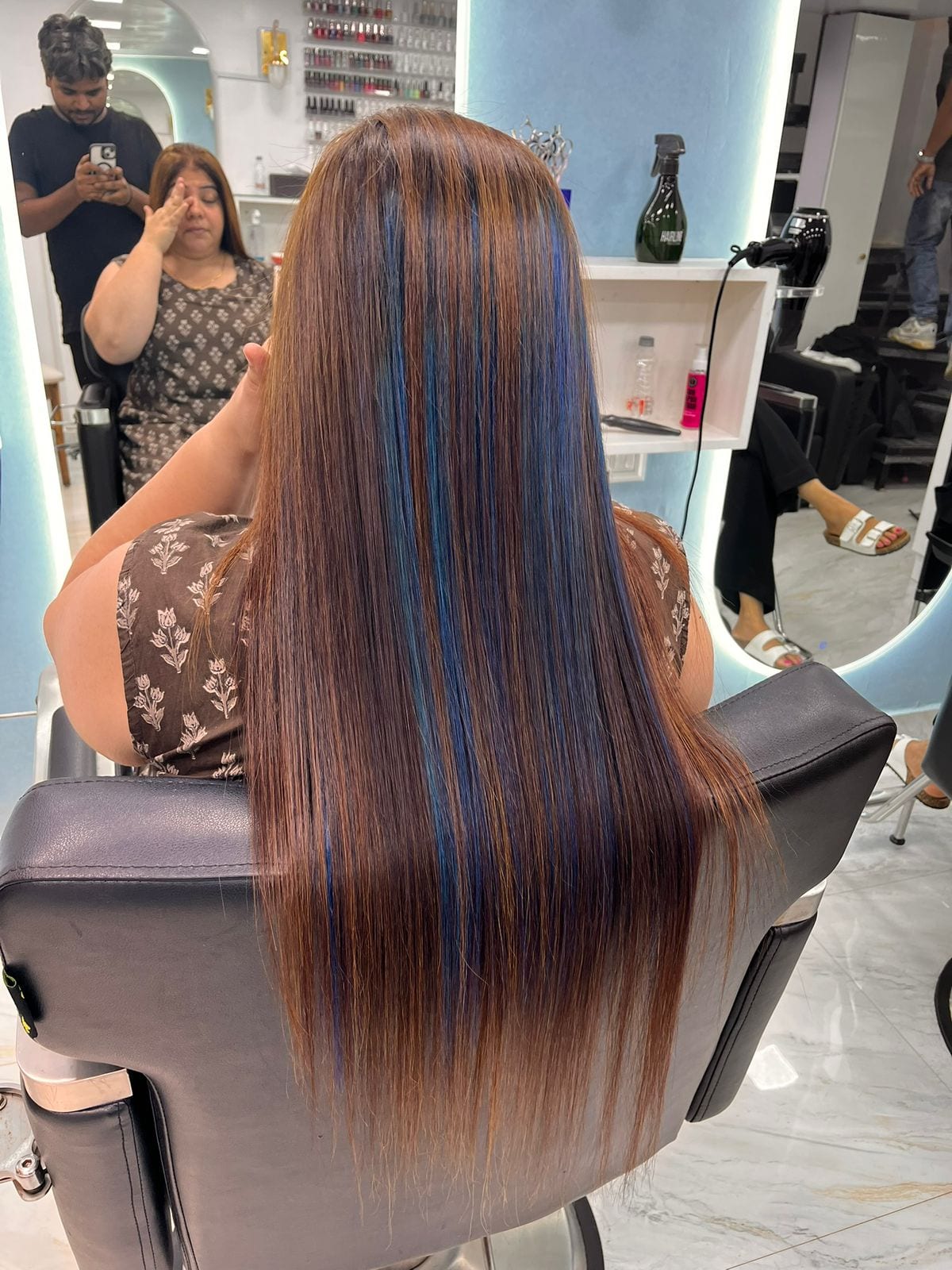 Stylist working on a client's long straight brown hair in the salon