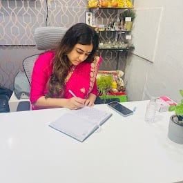 Woman writing at a desk in the shop interior with shelves of products behind her