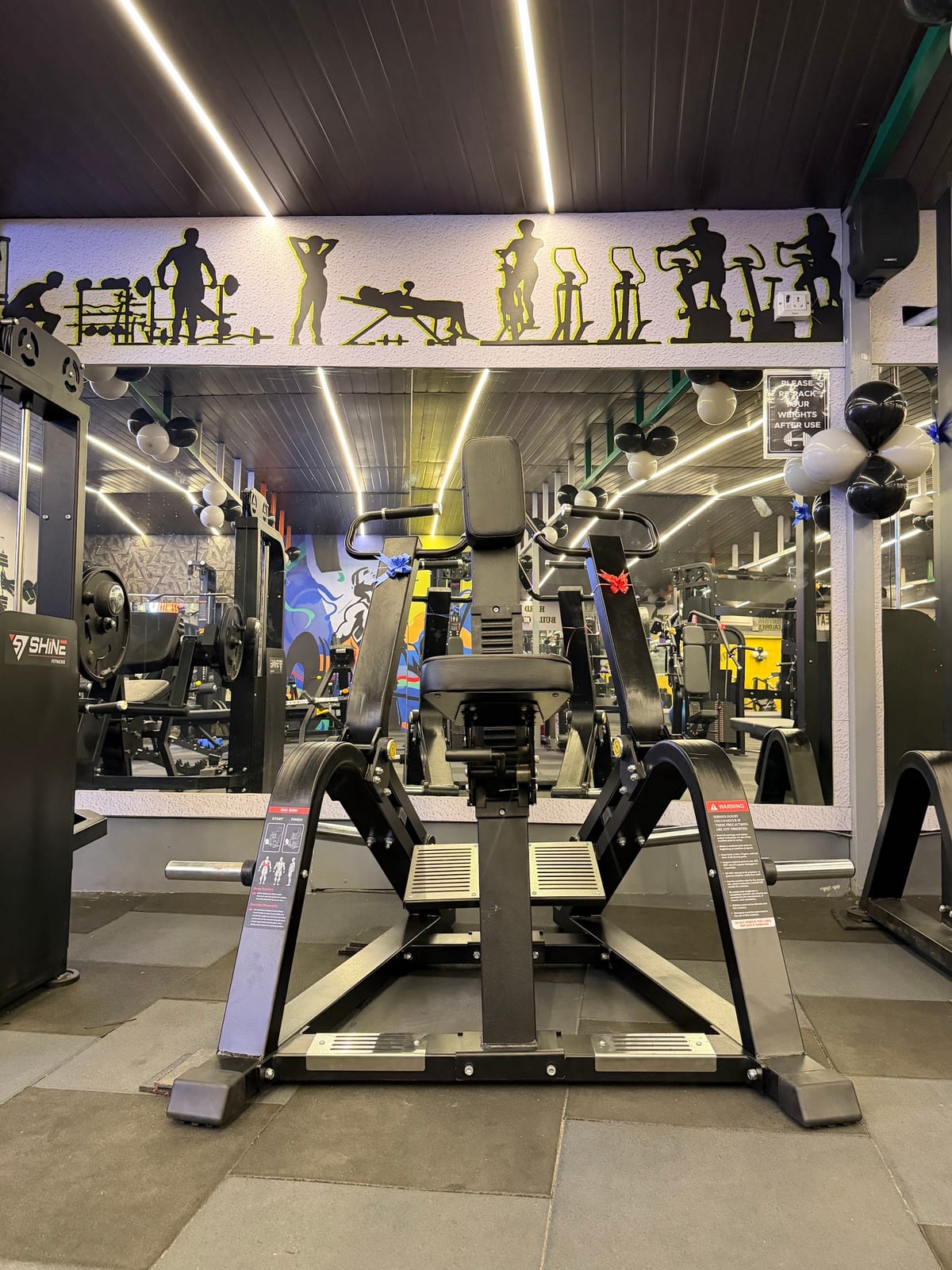 Treadmills and exercise machines, with fitness art on yellow-accent walls, in a mirrored gym