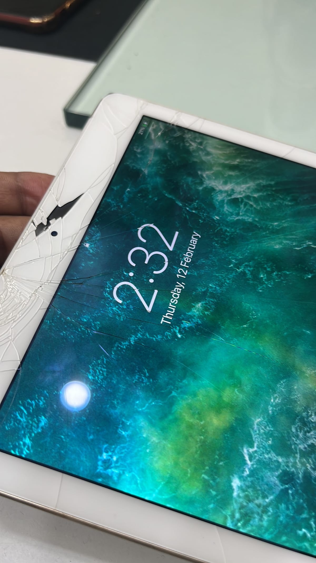 White tablet with an extensively cracked screen showing an ocean lock screen