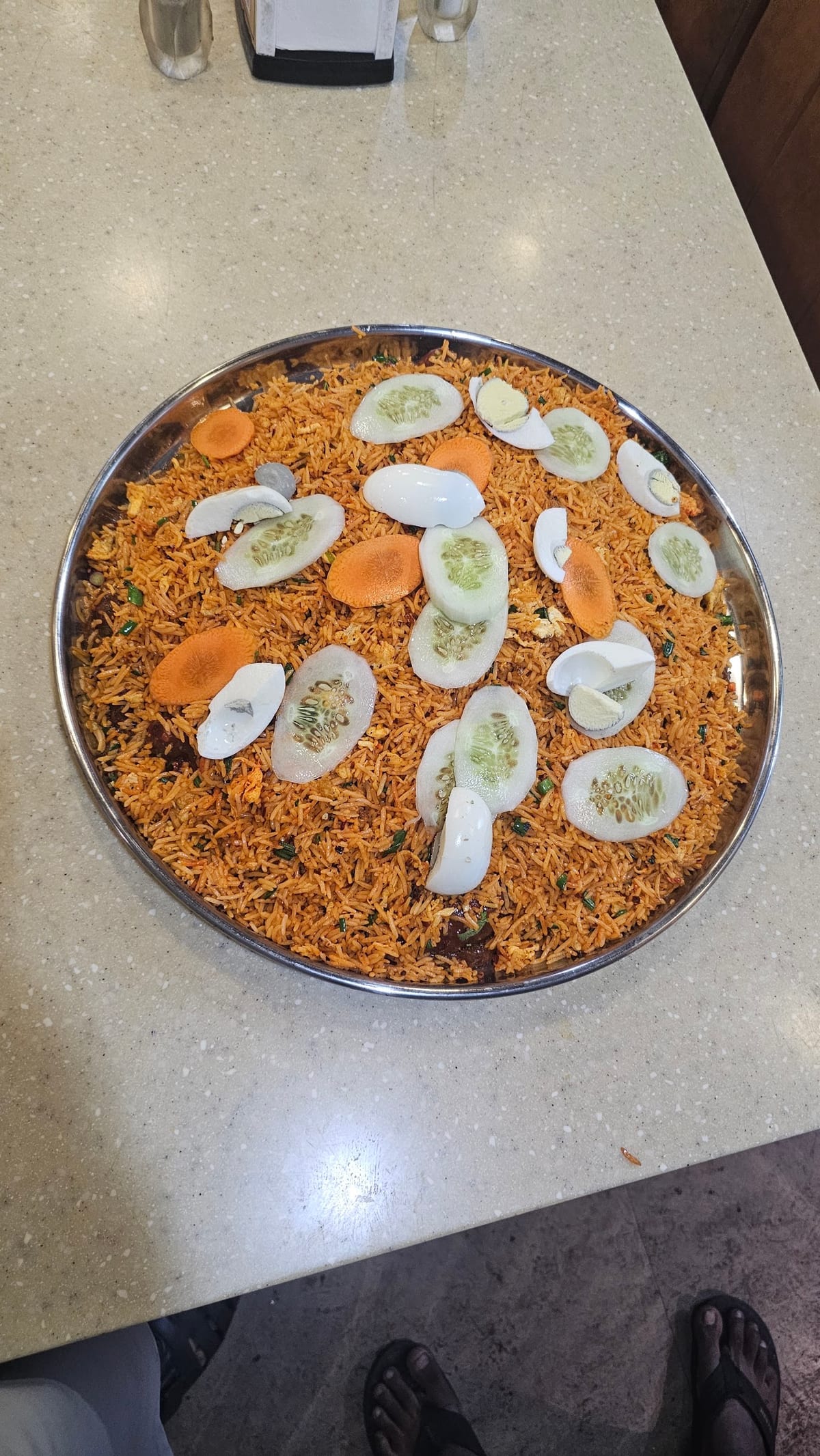 Round platter of orange biryani rice topped with sliced vegetables and white pieces