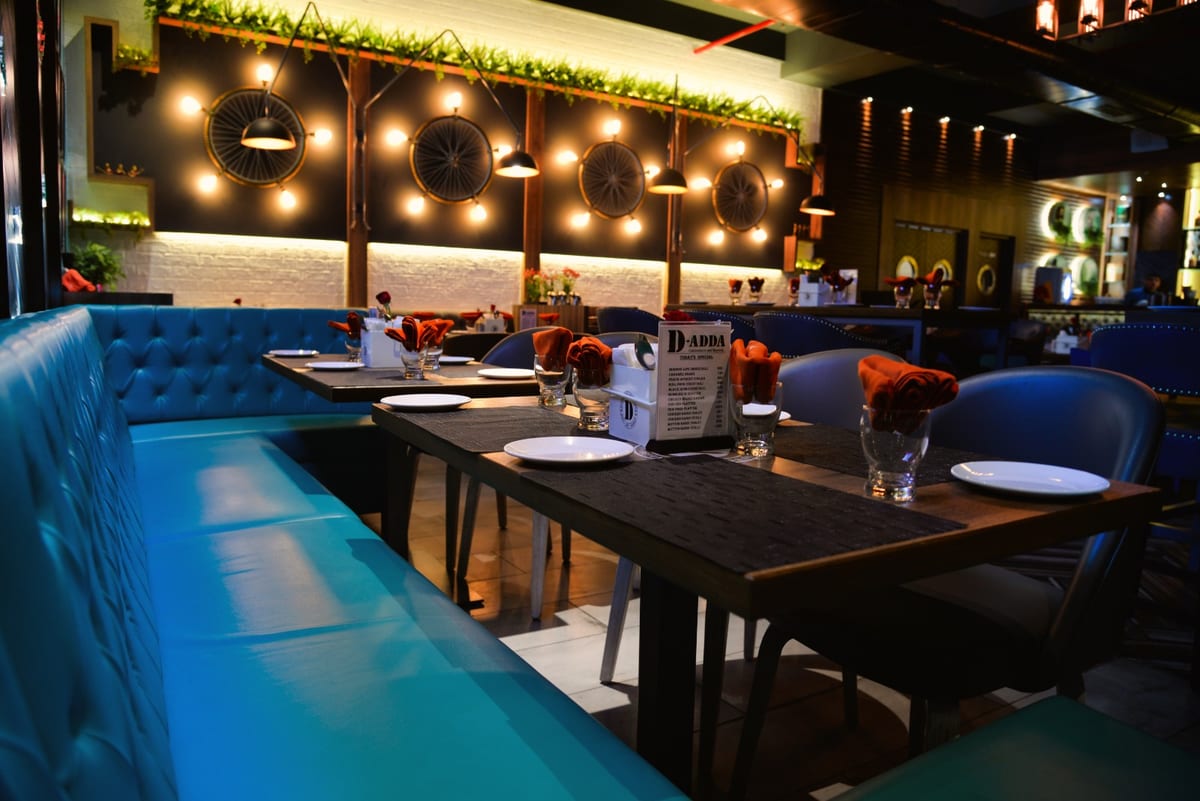 Restaurant dining area with blue upholstered booths, set tables and decorative greenery