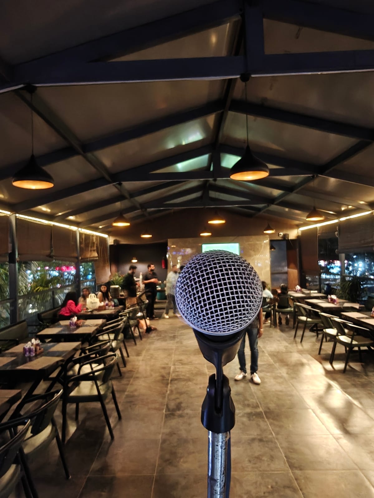 Covered dining area with tables, chairs, pendant lights and a microphone in the foreground
